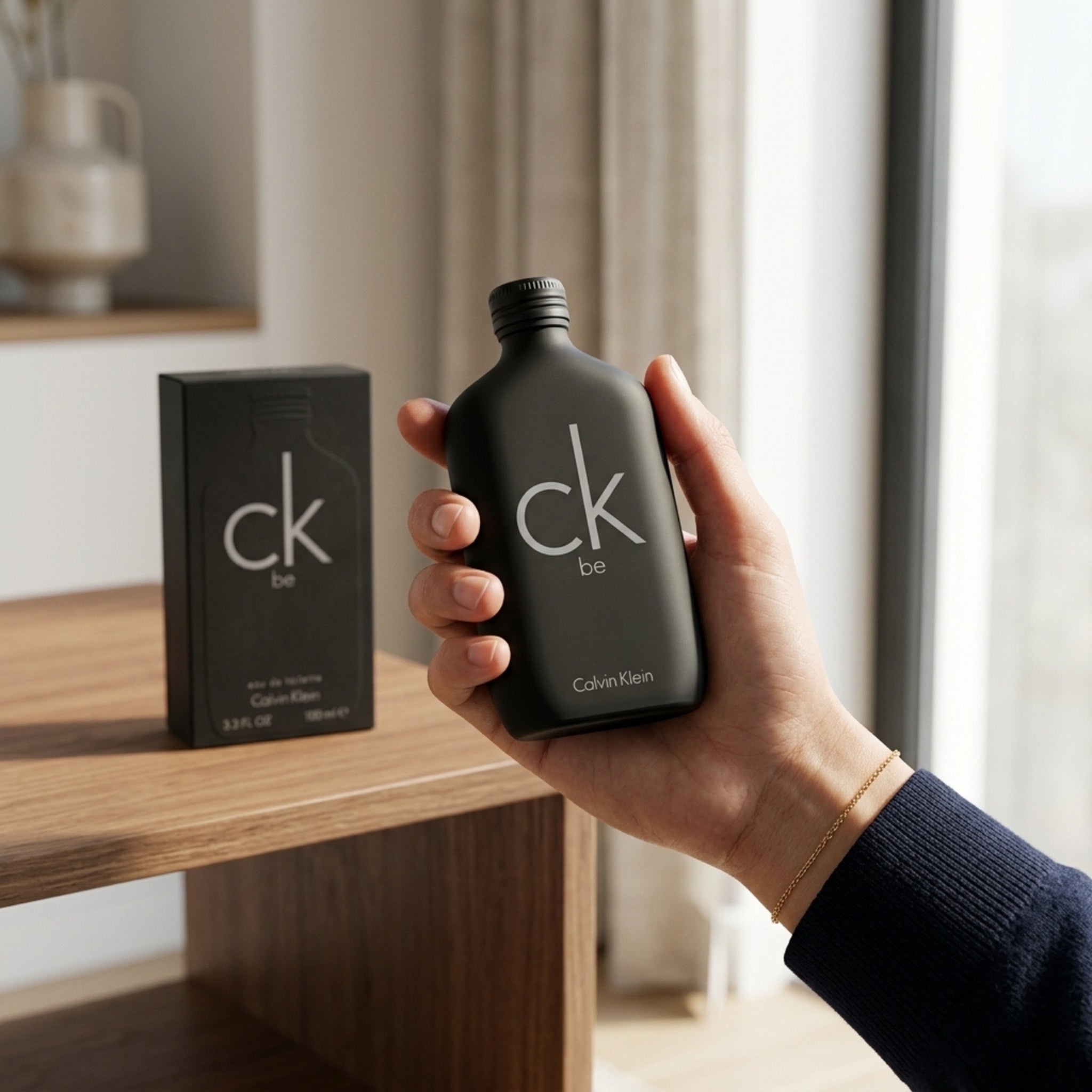 Hand holding Calvin Klein CK Be perfume bottle with box in background lifestyle shot