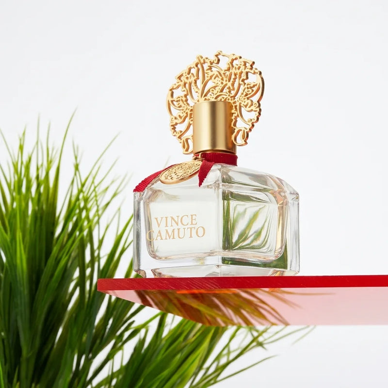 Vince Camuto perfume bottle with decorative gold cap against a pink and orange background